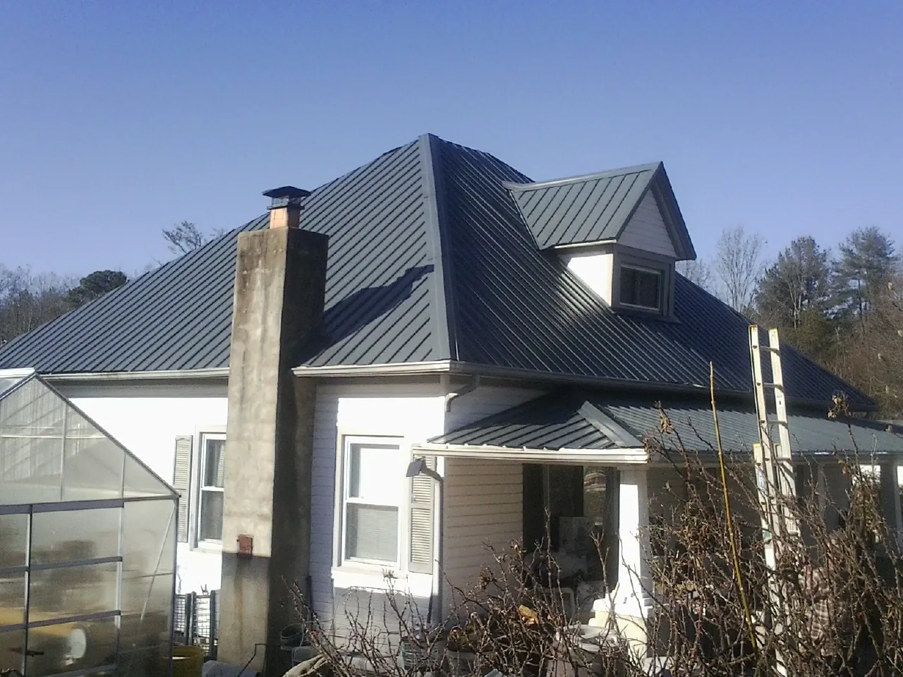 Dark blue standing seam metal roof on a white farmhouse with dormer — Slate & Tile Roof Repair by Roofing Brothers in Suncook