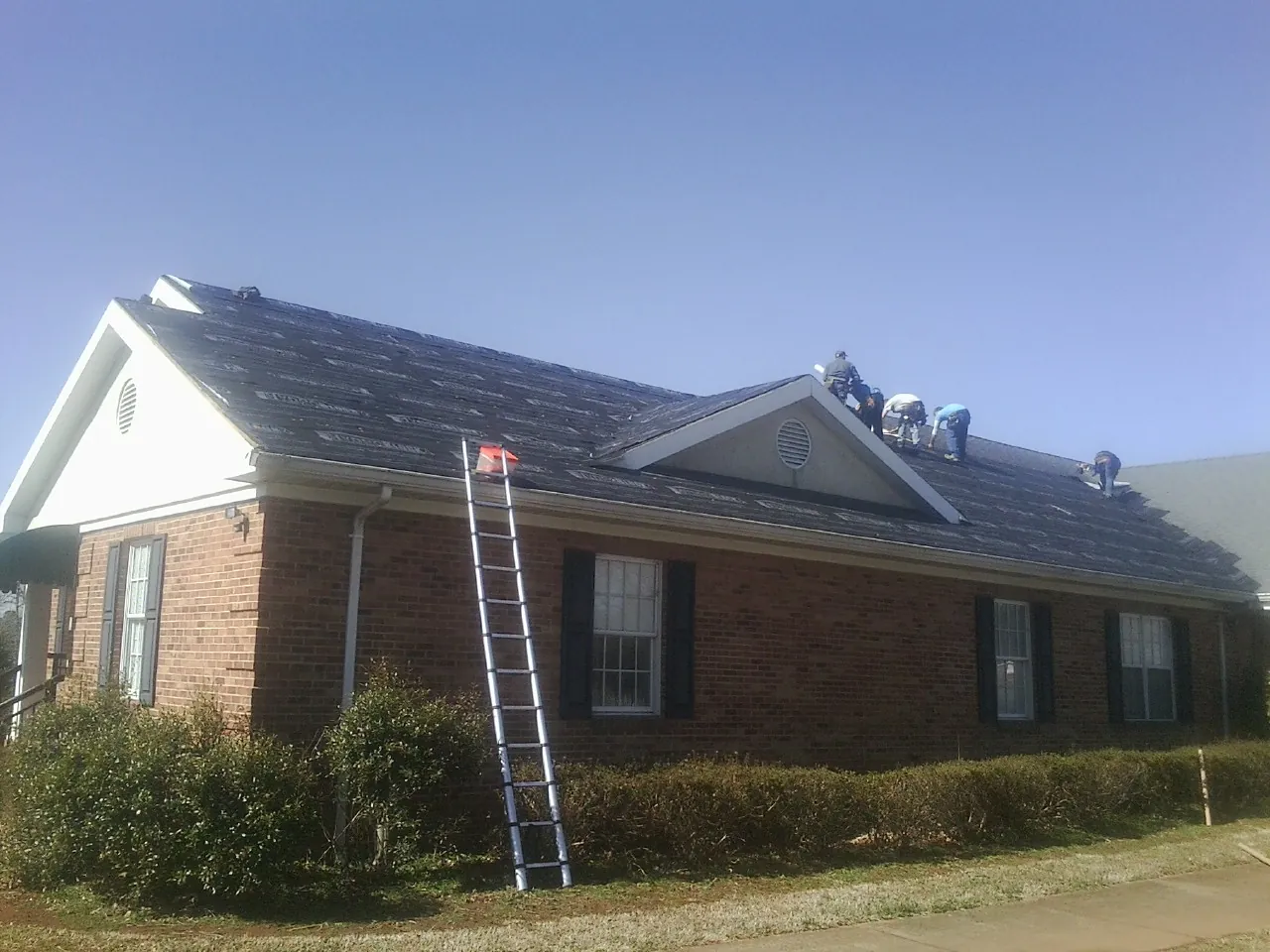 Crew tearing shingles off a brick ranch roof with a ladder set — Emergency Roof Repair work by our crew in Suncook