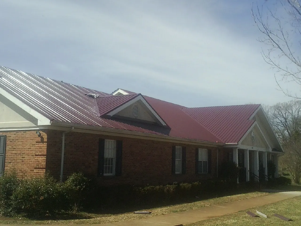 Red metal roof with gabled entries on a long brick building, from a Hail Damage Roof Repair job in Suncook