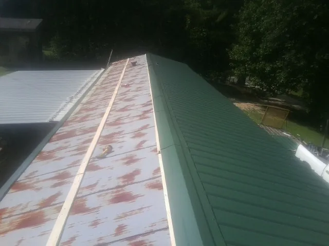 Old rusted panels beside newly installed green metal roofing — Wind Damage Roof Repair by Roofing Brothers in Suncook