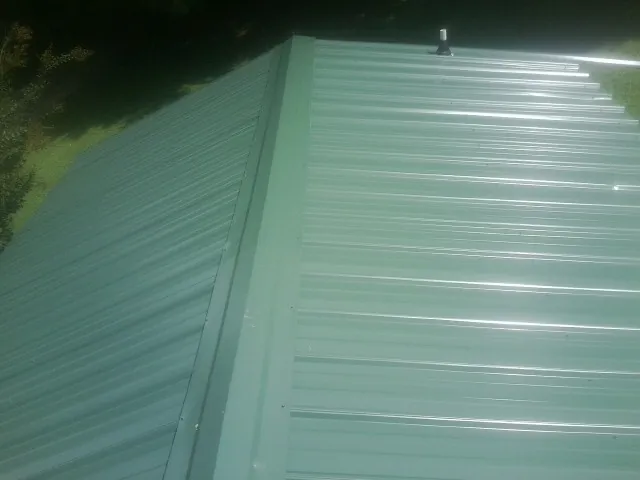 New green metal panels meeting at the ridge of a roof — Flat Roof Repair work by our crew in Suncook