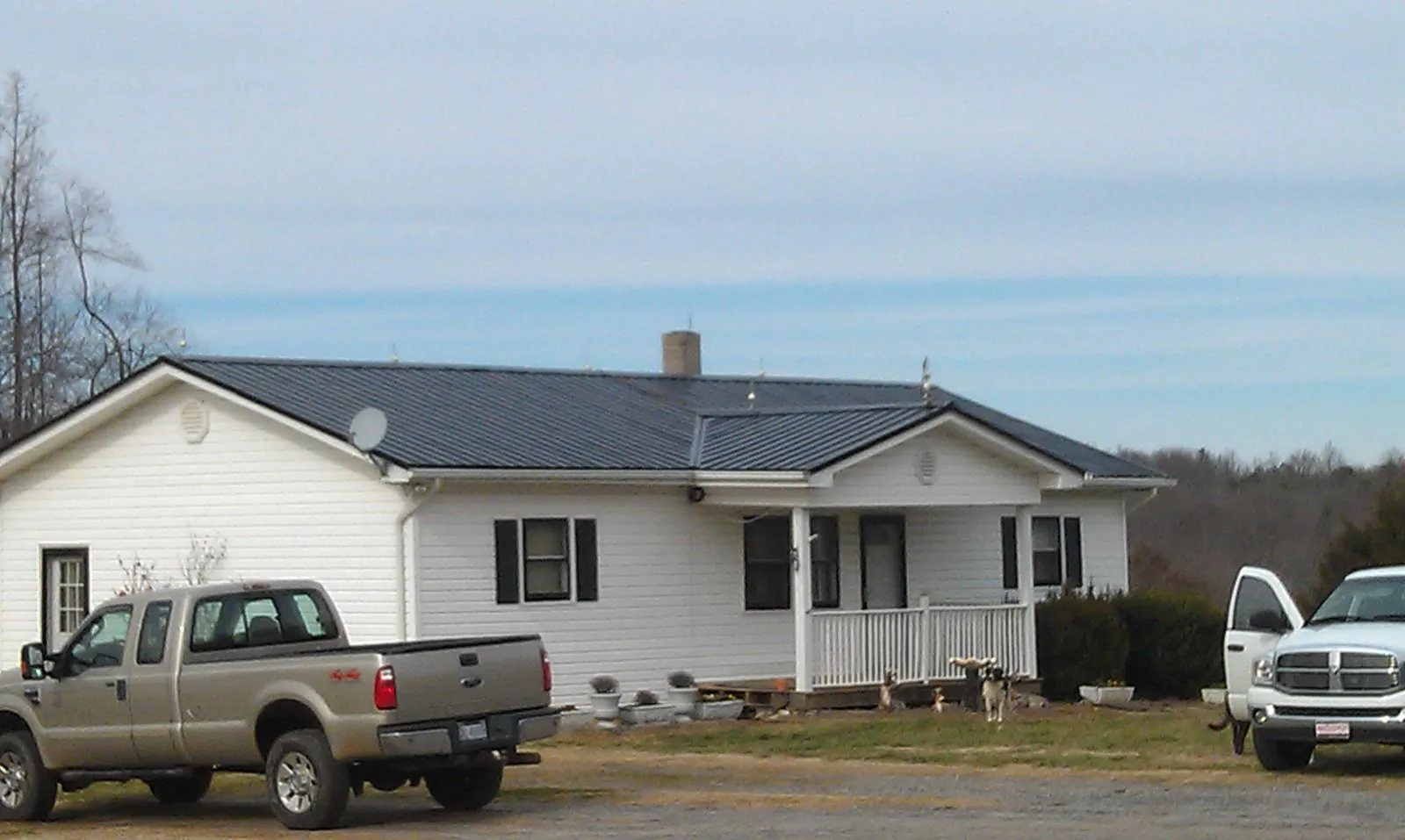 Finished dark metal roof on a white ranch home with work trucks parked in Suncook