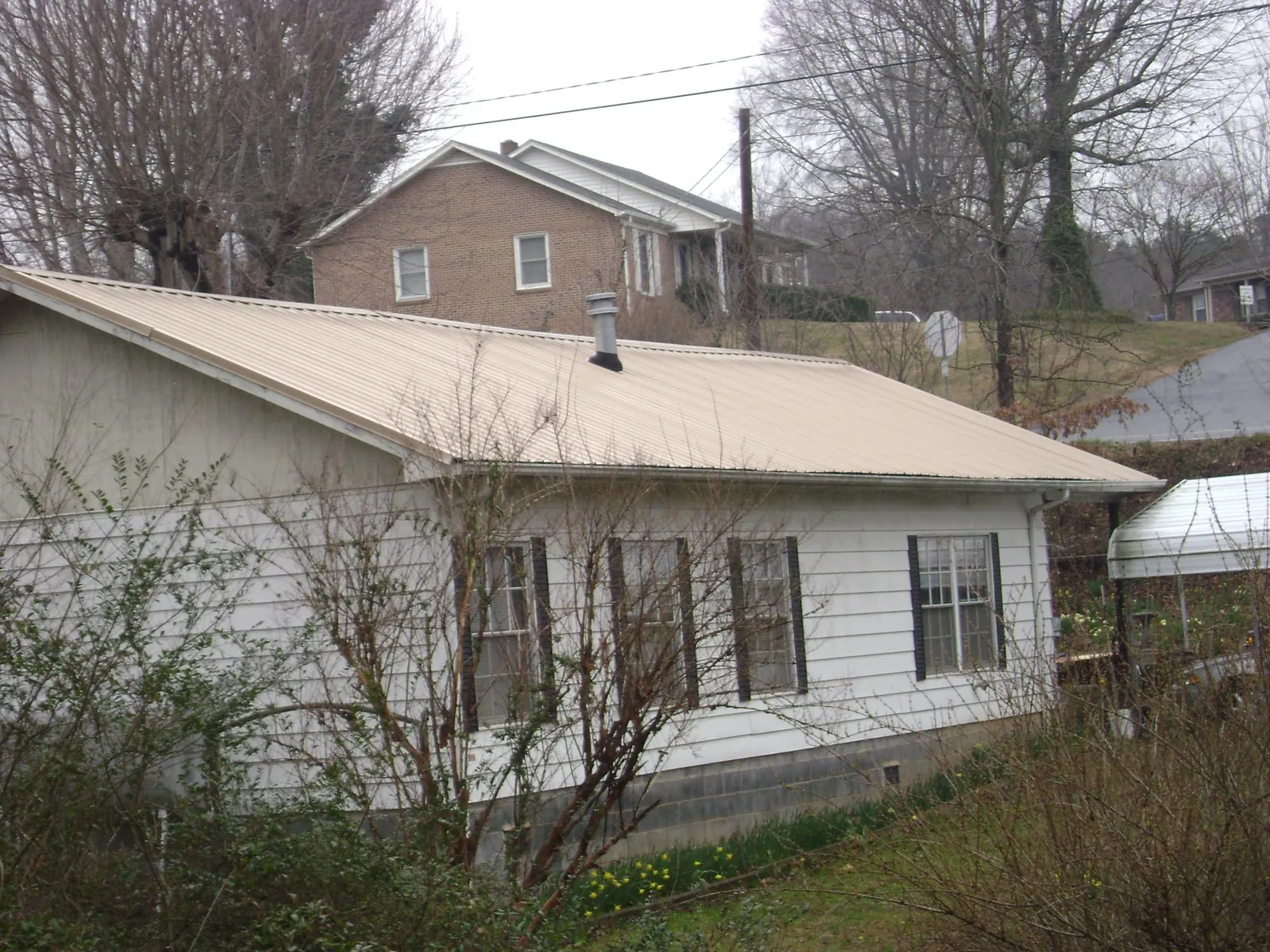 Tan metal roof on a white sided house set into a hillside — Commercial Roofing by Roofing Brothers in Suncook