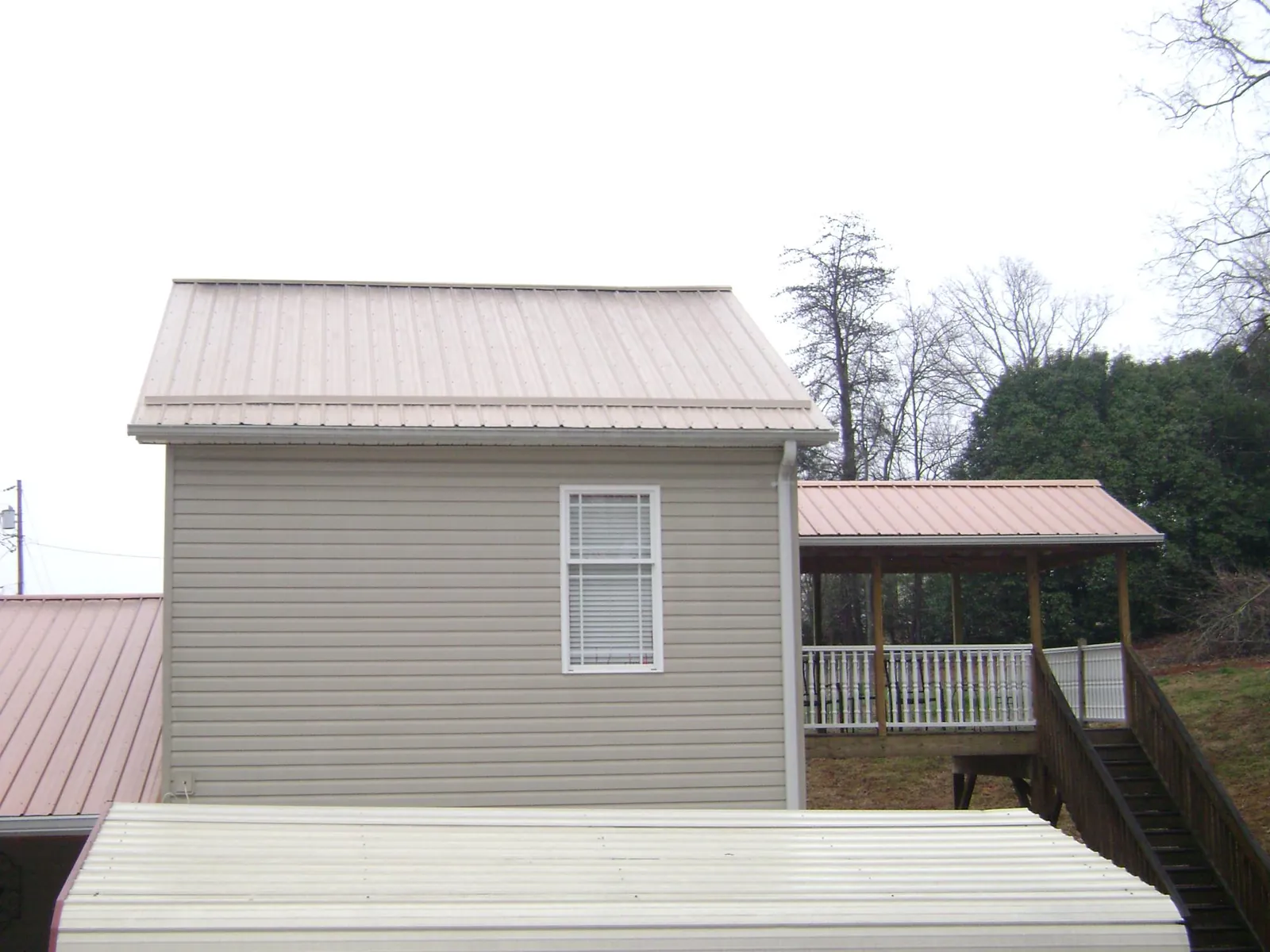 Tan metal roofs on a two story addition and attached porch, from a Roof Replacement job in Suncook