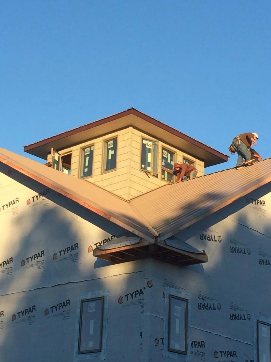 Roofers working around a rooftop cupola on a new metal roof at sunset — Roof Waterproofing in Suncook by Roofing Brothers